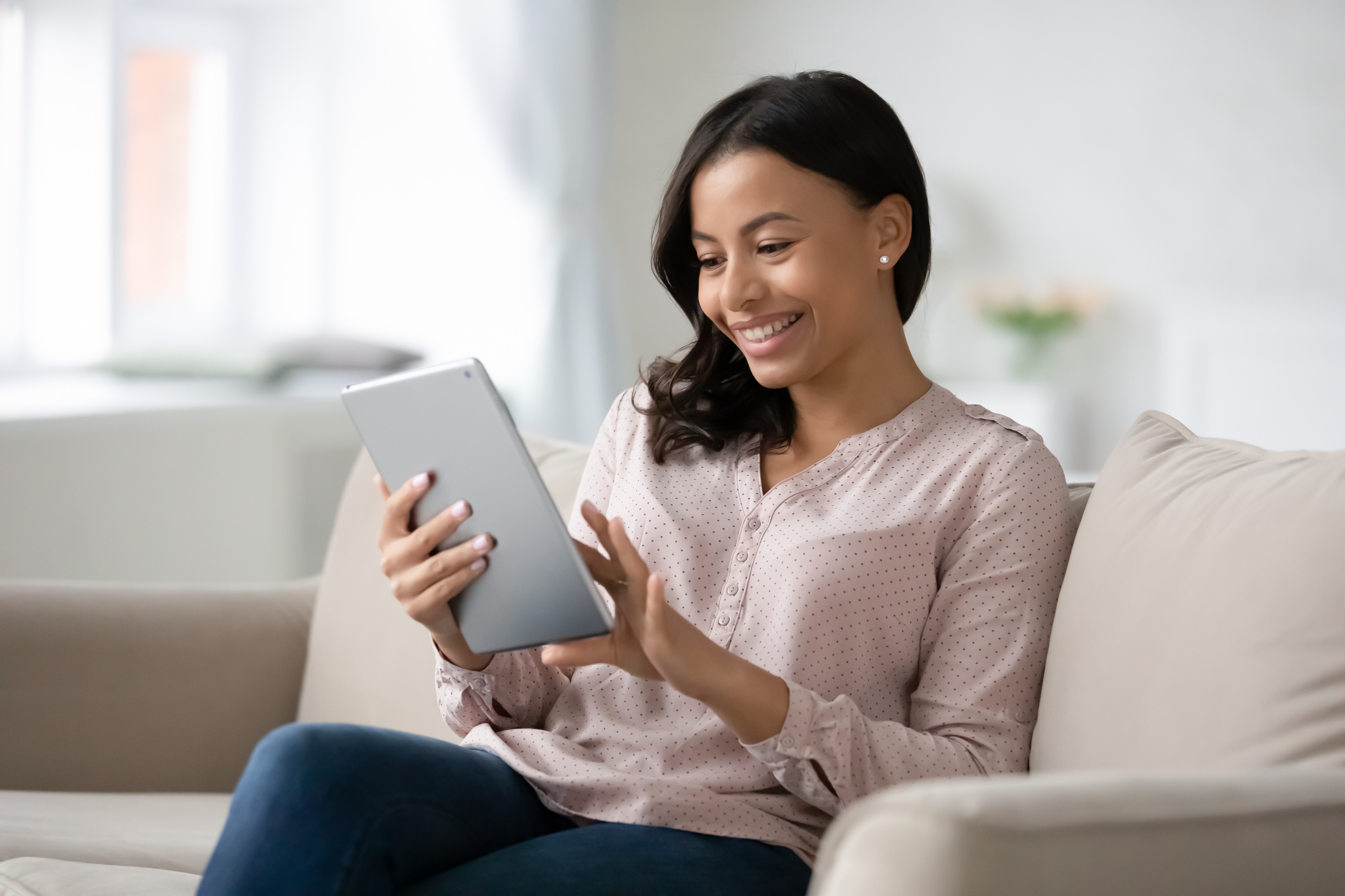 Woman smiling down at her tablet while sitting on couch. 