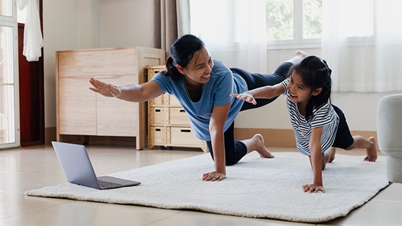 mother and daughter do yoga stretch on mat with laptop on floor