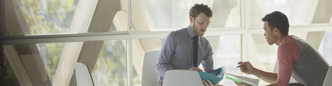 Two coworkers sitting and discussing project while looking through folders