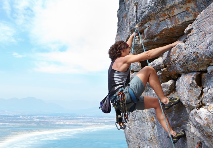 Rock climber scaling cliff with beach in distance