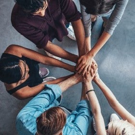 Overhead shot of people standing in circle putting their hands together in the middle of the circle