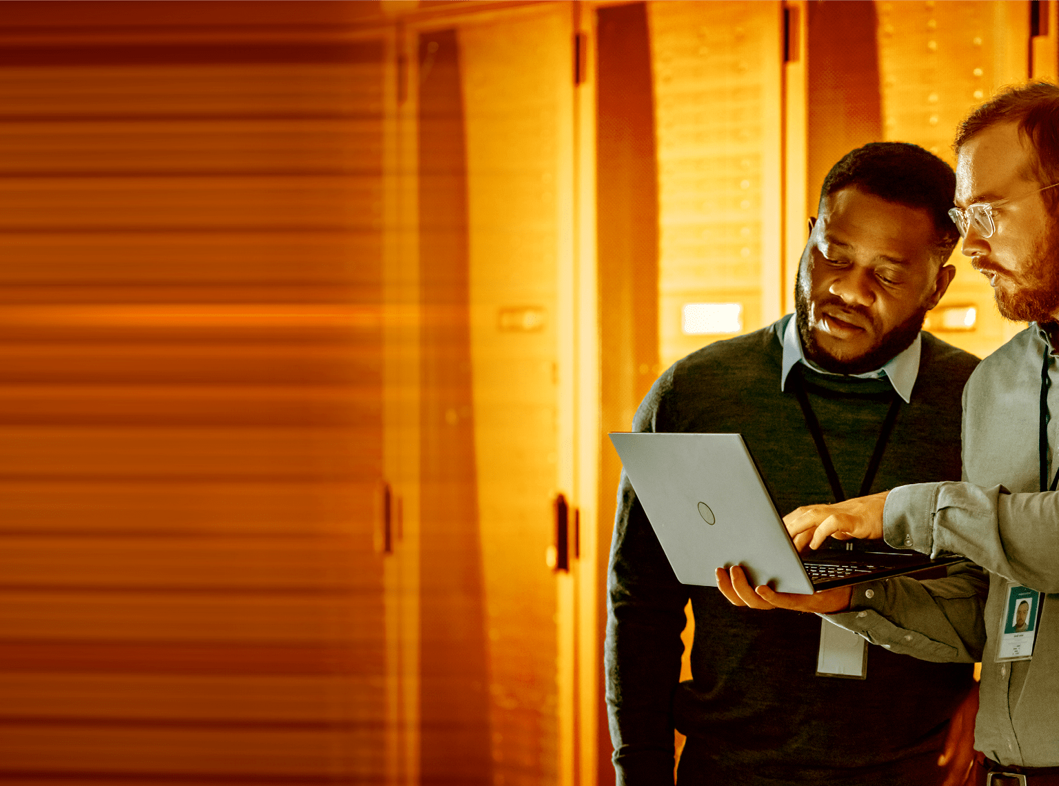 Two i t workers looking at a laptop in a server room