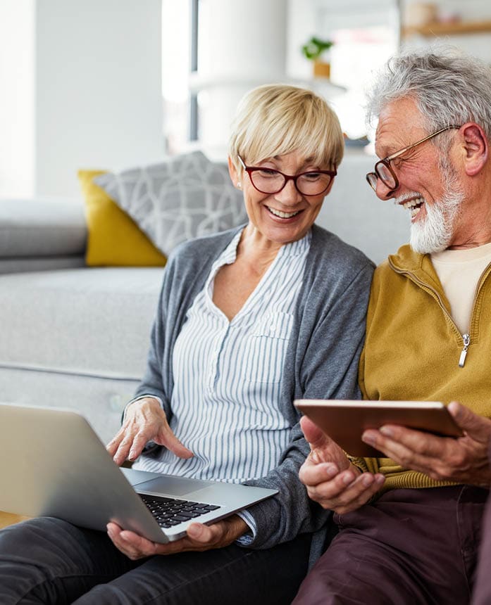 Middle aged man and woman smiling at each other while holding computer and tablet