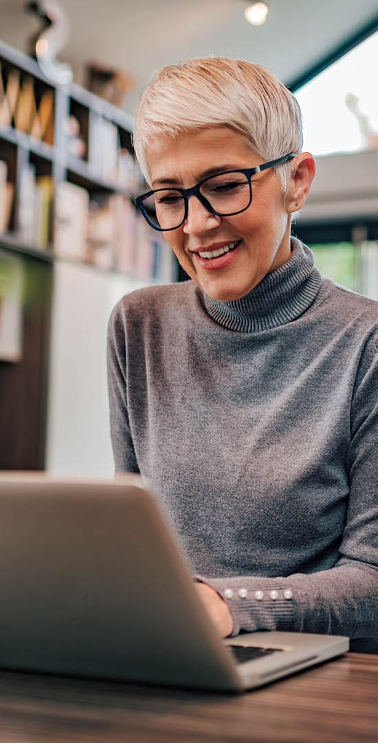 Image of an older woman smiling while on her laptop.